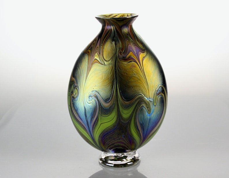 May include: A round glass vase with a swirling pattern of green, blue, and gold. The vase has a clear glass base.