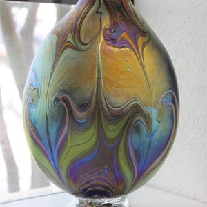 May include: A large, iridescent glass vase with a swirling pattern of blue, green, gold, and purple. The vase has a round body and a clear glass base.