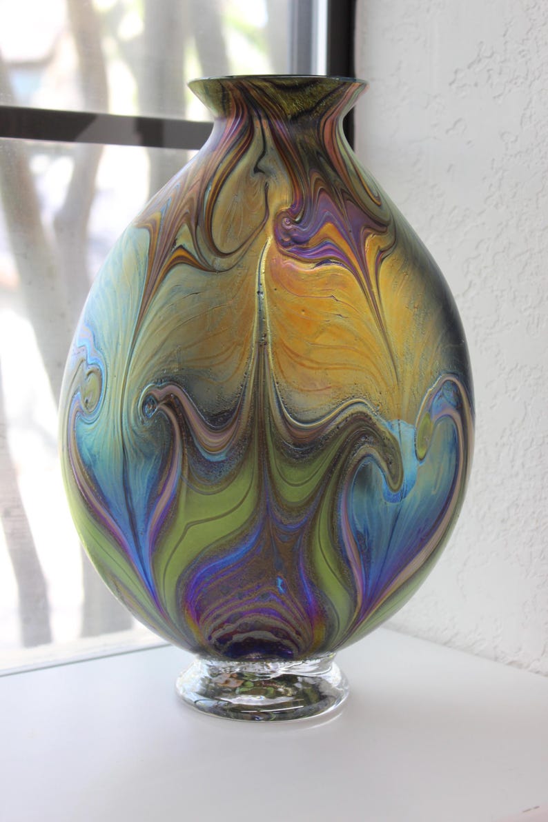 May include: A large, iridescent glass vase with a swirling pattern of blue, green, gold, and purple. The vase has a round body and a clear glass base.