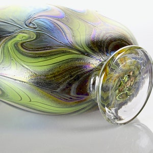 May include: A green and black iridescent glass vase with a swirling pattern. The vase has a clear glass base.