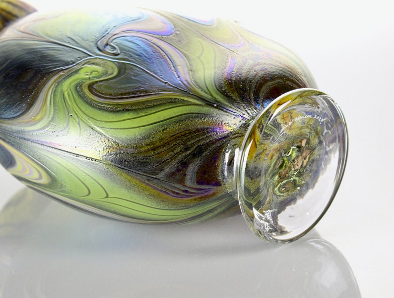 May include: A green and black iridescent glass vase with a swirling pattern. The vase has a clear glass base.