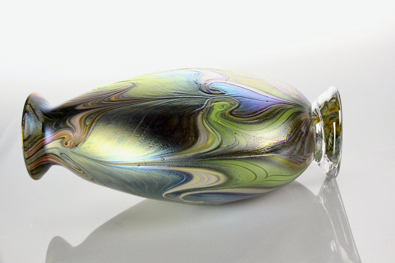 May include: A small, iridescent glass vase with a swirling pattern of green, blue, and gold. The vase has a rounded body and a narrow neck.