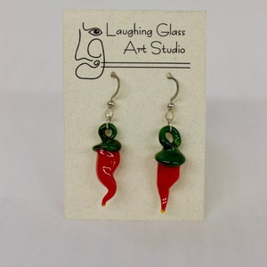 May include: A pair of red and green glass chili pepper earrings with silver hooks. The earrings are on a white card with the text "Laughing Glass Art Studio".