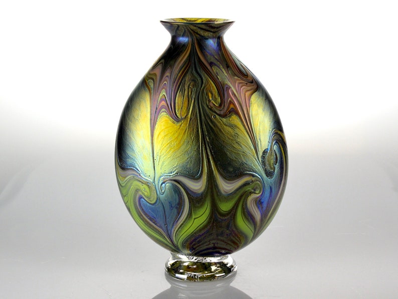 May include: A round iridescent glass vase with a swirling pattern of blue, green, yellow, and purple. The vase has a small, clear glass base.