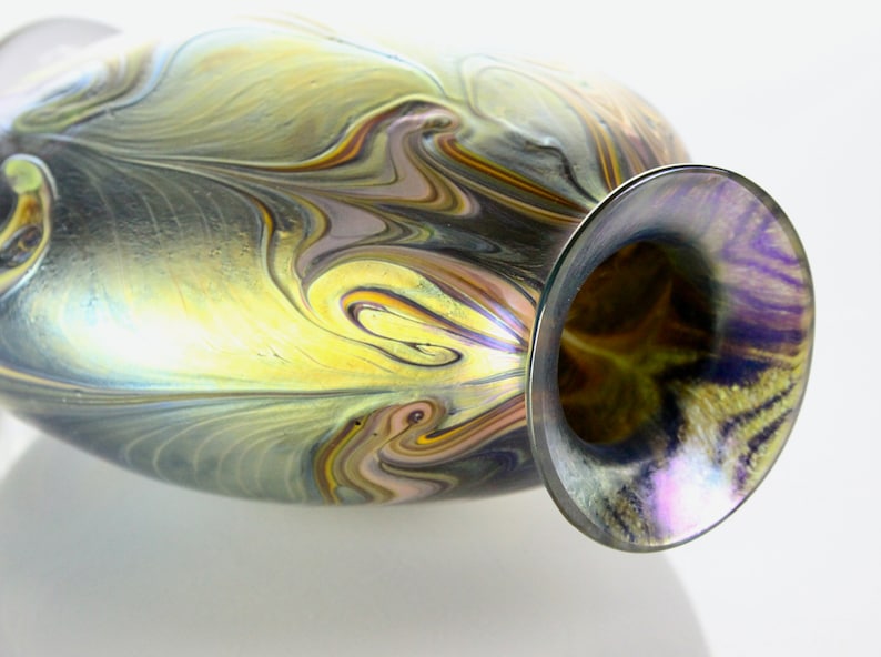 May include: A glass vase with a swirling pattern of gold, brown, and purple iridescent glass. The vase has a wide mouth and a narrow neck.