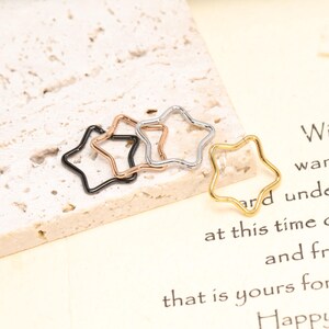 May include: Four open star-shaped rings in different metallic finishes, including black, rose gold, silver, and gold. Each star ring features a thin, continuous wire frame with a small opening, designed as a circular hoop component for jewelry making.