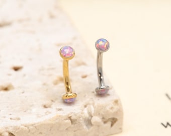 Könnte beinhalten: Zwei gebogene Piercing-Stäbe mit runden, schillernden, rosa opalfarbenen Steinen an beiden Enden. Ein Stab hat ein goldfarbenes Metall-Finish, während der andere ein silberfarbenes Metall-Finish aufweist. Beide Schmuckstücke haben einen gebogenen Schaft.