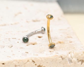 Könnte beinhalten: Zwei gebogene Barbell-Piercings, eines aus silberfarbenem und eines aus goldfarbenem Metall. Jedes Barbell verfügt über einen kleinen, runden, dunkelgrünen Stein an beiden Enden des gebogenen Stabs, was ein einheitliches Design für beide Artikel ergibt.