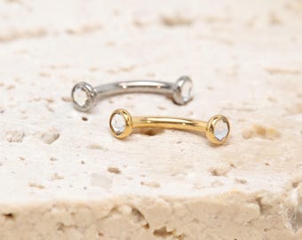 Könnte beinhalten: Zwei gebogene Piercing-Stäbe, einer in Silberoptik und einer in Goldoptik. Jeder Stab ist an beiden Enden mit einem kleinen, klaren, runden Schmuckstein besetzt, die auf dem gebogenen Metallsteg angebracht sind und ein klares Design bieten.