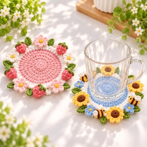 May include: Two round crochet coasters. One features a pink center with a border of pink flowers, green leaves, and red strawberries. The other features a light blue center with a border of yellow sunflowers, blue flowers, green leaves, and bees.