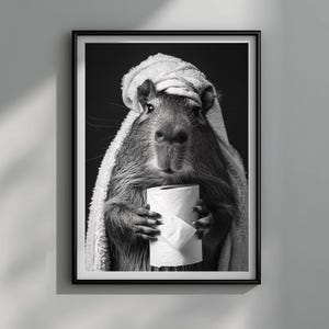 May include: Black and white framed print featuring a capybara wrapped in a towel, holding a roll of toilet paper. The capybara is the central focus, with a dark background. The image is a humorous take on self-care and relaxation.