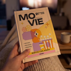 May include: A movie log book titled "Movie Festival" with a colourful cover design. The cover features illustrations of popcorn, a drink, and a stylized face. The book includes sections for movies, reviews, and debates, with the year 2026.