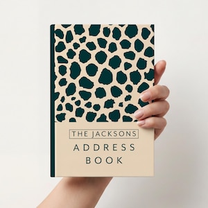 Peut inclure: Un carnet d'adresses crème avec un motif tacheté vert foncé sur la couverture. La tranche est vert foncé. Le texte "THE JACKSONS ADDRESS BOOK" est imprimé dans un encadré en bas de la couverture.