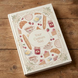 Puede incluir: Un libro de tapa dura con cubierta blanca que presenta un borde ornamentado y un patrón de artículos de desayuno que incluyen croissants, baguettes, tazas de té, tarros de mermelada, mantequilla y fresas. El centro contiene el texto Your Custom Text.