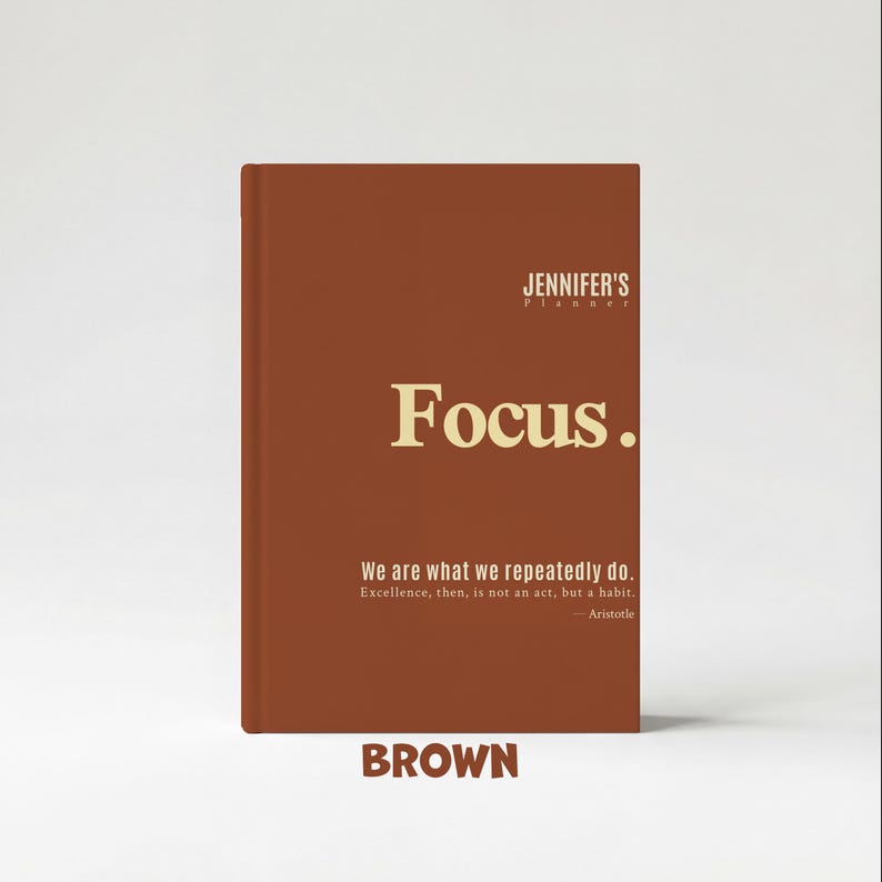 May include: A brown planner with the text "Focus." in gold lettering. The planner also features the text "We are what we repeatedly do. Excellence, then, is not an act, but a habit. - Aristotle" and the word "BROWN".