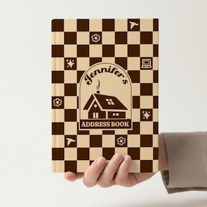 Könnte beinhalten: Ein braunes und beiges Adressbuch mit Schachbrettmuster. Das Cover zeigt eine Hausillustration mit dem Text "Jennifer's Address Book". Dekorative Elemente sind Blumen, Sterne und ein Computersymbol.