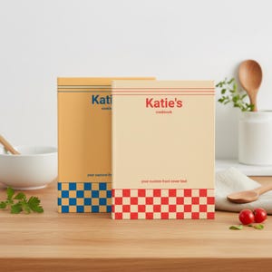 Könnte beinhalten: Zwei gebundene Kochbücher in rechteckiger Form. Das linke Buch ist gelb mit blauem Text, der Katie's cookbook lautet, und einem blauen Schachbrettmuster am unteren Rand. Das rechte Buch ist cremefarben mit rotem Text, der Katie's cookbook lautet.