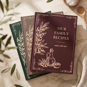 Könnte beinhalten: Drei Rezeptbücher mit festem Einband in Dunkelgrün, Taupe und Dunkelrot. Jedes ist mit goldenen Illustrationen von Olivenzweigen, einer Ölkanne und einer Schale mit Oliven verziert. Der dunkelrote Einband trägt den Text OUR FAMILY RECIPES made with love.