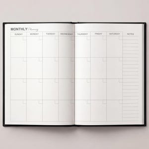 May include: Open black notebook with a monthly planning layout. The left page displays a calendar grid with days of the week across the top. The right page has a notes section. The words "MONTHLY Planning" are at the top.