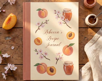 May include: A hardcover recipe journal with a cream-colored cover featuring illustrations of peaches, peach blossoms, and jars of jam. The text "Rebecca's Recipe Journal" is printed in the center in a brown script font. The spine is a solid terracotta color.