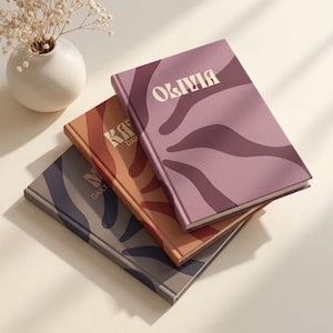 May include: Three stacked hardback journals featuring abstract wavy patterns in shades of mauve, terracotta, and slate grey. The top journal displays the name OLIVIA in cream lettering, while the others show partial text including DAILY.