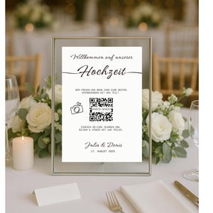 Könnte beinhalten: Ein gerahmtes Hochzeitsschild mit dem Text "Willkommen auf unserer Hochzeit" in eleganter Schrift. Das Schild enthält einen QR-Code und die Namen "Julia & Denis" mit dem Datum 17. August 2009. Umgeben von weißen Blumen und Kerzen.