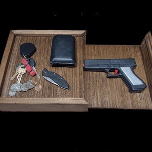 May include: A wooden tray with a black wallet, a set of keys, a pocket knife, and a black and silver toy gun. The tray has a sliding drawer.