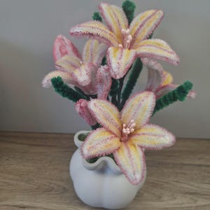 Peut inclure: Un bouquet de fleurs faites à la main dans un vase en céramique blanc. Les fleurs ont des pétales jaunes et roses avec des tiges vertes. Le vase présente un design ondulé unique.