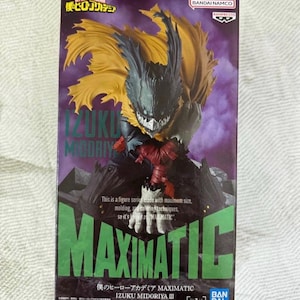 May include: A boxed MAXIMATIC figure of Izuku Midoriya from My Hero Academia. The figure has a detailed design with a black and yellow cape, and the box features green and purple text.