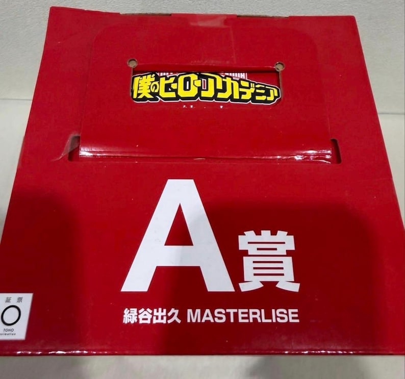 May include: A bright red rectangular cardboard box featuring the My Hero Academia logo in yellow and black at the top. The front displays a large white letter A followed by the Japanese characters for prize, and the text Midoriya Izuku MASTERLISE.