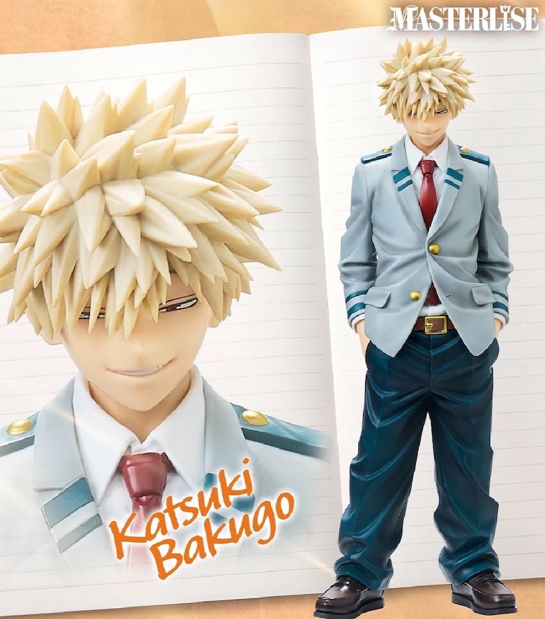 May include: A Katsuki Bakugo figure from the anime series. The figure has spiky blonde hair, a light blue blazer with green accents, a red tie, and dark blue pants. The figure is standing with hands in pockets. The name "Katsuki Bakugo" is printed on the notebook.