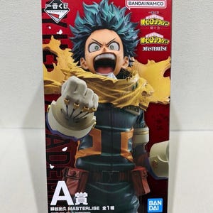 May include: A collectible anime figure box featuring Izuku Midoriya from My Hero Academia. The box displays the character with spiky teal hair, a yellow scarf, and a dark green suit with orange accents. Text includes Ichiban Kuji, Bandai Namco, and Masterlise.