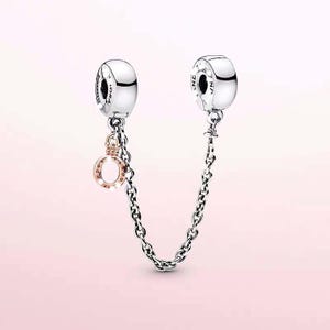 Può includere: Catena di sicurezza per bracciale argentata con due ciondoli cilindrici e una catena. Un ciondolo ha un ciondolo color oro rosa con la scritta "Pandora". L'altro ciondolo ha la scritta "Pandora". Lo sfondo è rosa tenue.