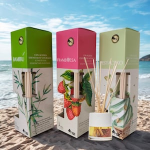 Puede incluir: Tres cajas rectangulares de difusores de varillas en verde, rosa y verde claro, con ilustraciones de bambú, frambuesas y pistachos. Un pequeño frasco de vidrio con tapa blanca y varillas de madera se sitúa delante, conteniendo líquido ámbar.
