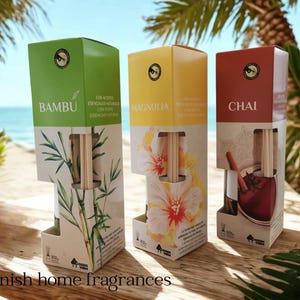 Peut inclure: Trois diffuseurs de parfum d'ambiance présentés dans des boîtes vertes, jaunes et rouges, avec les noms "Bambu", "Magnolia" et "Chai". Chaque boîte présente un design unique et le texte "Spanish home fragrances". Les diffuseurs sont sur une surface en bois, avec une plage en arrière-plan.