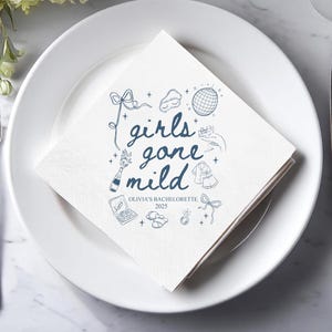 May include: White square paper napkin with blue illustrations and text. The text reads "girls gone mild" with additional drawings of a disco ball, champagne bottle, and other party-themed icons. The text "Olivia's Bachelorette 2025" is also included.