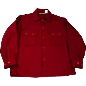 May include: A solid red button-down shirt with two chest pockets and buttoned cuffs. The long-sleeved shirt has a classic collar and buttons down the front. The shirt is made of a soft, possibly wool, material.