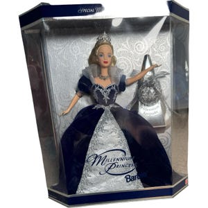Può includere: Bambola Barbie in una vetrina trasparente. La bambola indossa un abito blu scuro con dettagli argentati e una tiara. La confezione presenta le scritte "Millennium Princess" e "Millennium Keepsake".
