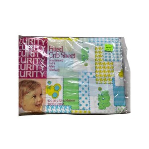 May include: A packaged fitted crib sheet with a patchwork design. The sheet features a pattern of green, blue, and yellow squares with cartoon animals and stars. The packaging includes the brand name "Curity" and the text "For 71 x 132 cm Mattress 100% Cotton."