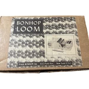 May include: A cardboard box featuring the text "BONHOP LOOM" in a bold, sans-serif font. Below the text is a black and white patterned design. A diagram of a loom is in the lower right corner. The box also includes the text "PAUL BONHOP, Inc 4132 Park Ave. New York 57.N.Y."