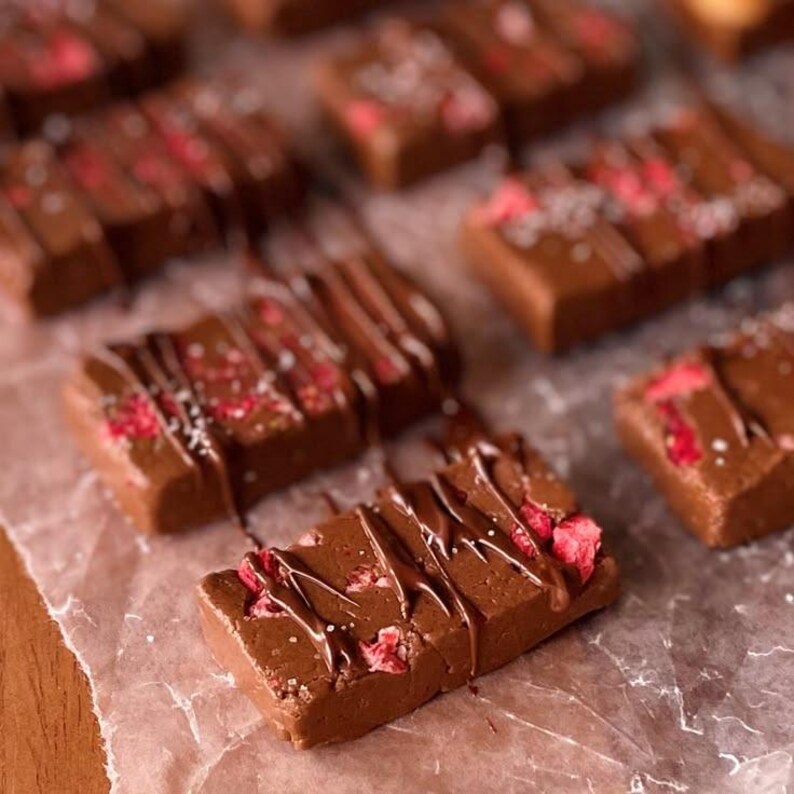 Op de afbeelding: Rechthoekige chocoladerepen belegd met gevriesdroogde rode frambozenstukjes en besprenkeld met pure chocolade. Elke reep heeft een glad, effen bruin oppervlak en is gerangschikt op een vel doorschijnend, gekreukt bakpapier.