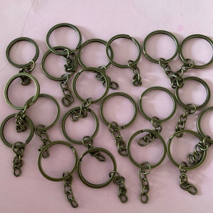 May include: A group of 15 antique gold key rings with attached chains. The key rings are all the same size and shape, and they are arranged in a random pattern on a pink surface.