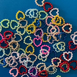 May include: A collection of colorful pearl rings in various shades of pink, red, yellow, blue, and green. The rings are arranged in a random pattern on a blue background.