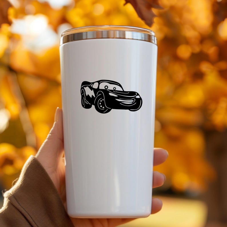 May include: White insulated tumbler with a silver lid. A black cartoon car graphic is displayed on the front. The car has a smiling face and lightning bolt details. The tumbler is designed to keep drinks hot or cold.