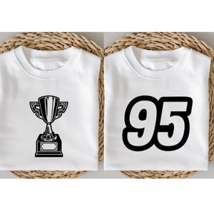 May include: Two white sweatshirts. One features a black trophy graphic, the other displays the number "95" in bold black font. Both shirts are folded and presented on a woven background, suitable for casual wear.