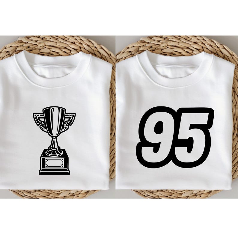 May include: Two white sweatshirts. One features a black trophy graphic, the other displays the number "95" in bold black font. Both shirts are folded and presented on a woven background, suitable for casual wear.