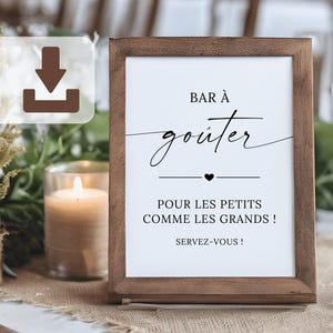 Op de afbeelding: Een houten lijst met de woorden "Bar à goûter" in elegant schrift, met de tekst "Pour les petits comme les grands !" en "Servez-vous !" in een bruine houten lijst. Een kaars en een decoratieve vaas staan op de achtergrond.
