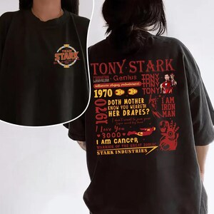 May include: Black t-shirt featuring the text "TONY STARK" and various phrases and graphics in red and white. The front of the shirt has a "TEAM STARK" logo. The shirt is a short-sleeved, casual style.