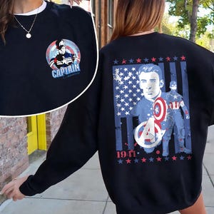 May include: Black sweatshirt featuring Captain America graphics. The front has a circular design with Captain America and the text "CAPTAIN AMERICA". The back displays a portrait, shield, and the year "1941" with stars and stripes.