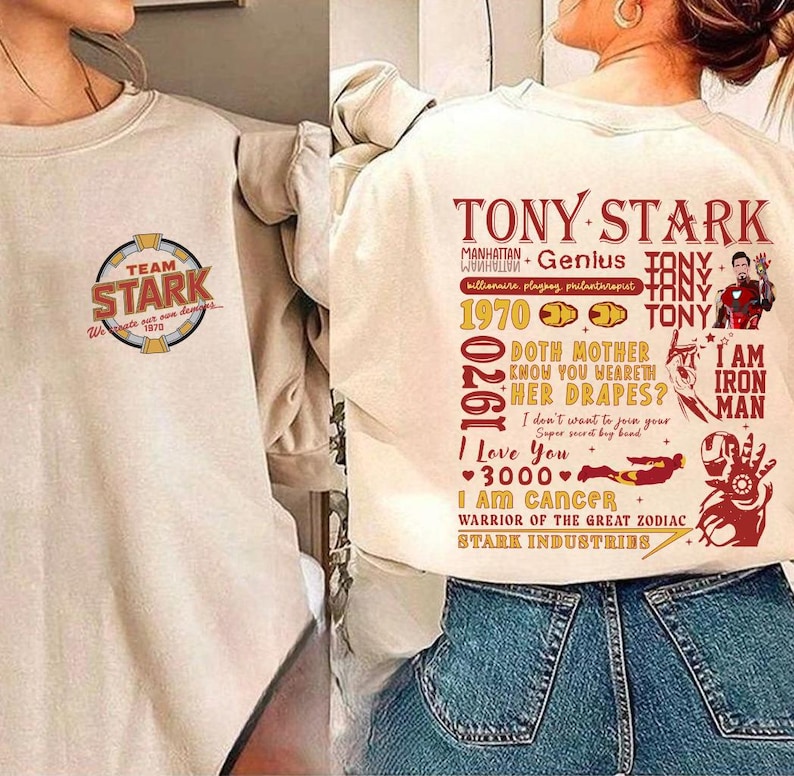 May include: Cream-colored sweatshirt with "TEAM STARK" logo and text. The back features a graphic with "TONY STARK" and other text, including "I AM IRON MAN" and "STARK INDUSTRIES".